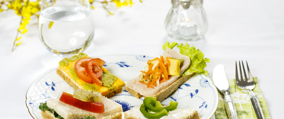 Fire stykker smørrebrød anrettet på tallerken med bestik