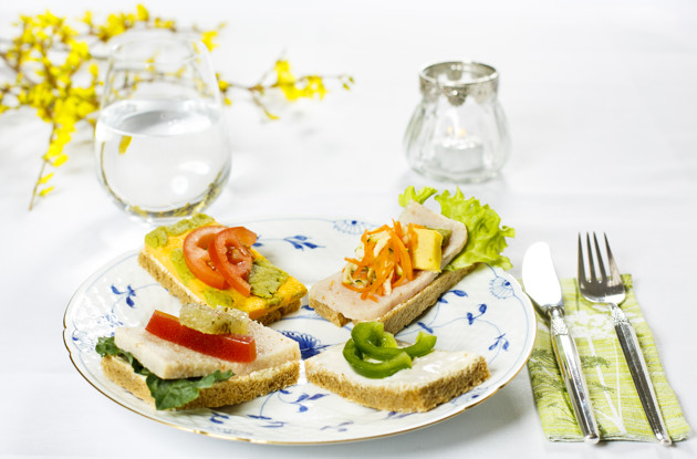 Fire stykker smørrebrød anrettet på tallerken med bestik